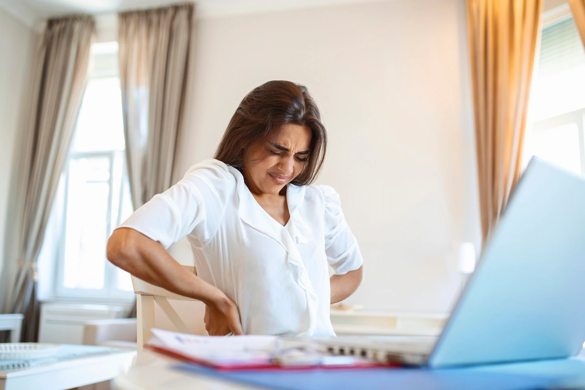 Female holding her back in pain sitting at desk