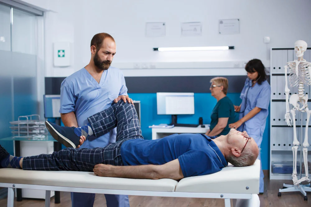 Chiropractor performing leg and hip adjustment therapy on senior patient in modern clinic